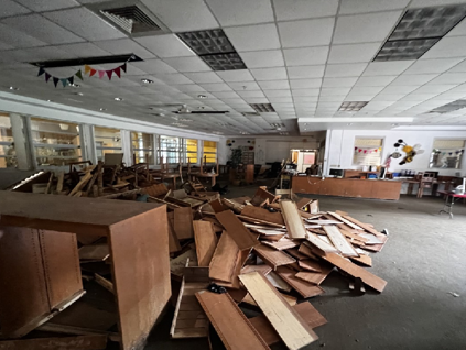 A library with broken shelves and chairs strewn across the room.