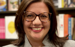 Jessica Ewing, the CEO and Founder of Literati, smiles at the camera before a shelf of books.