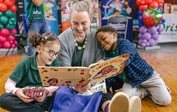 At a RIF Reading event, a seated women reads A Sofia Special to two children, a girl to her left and a boy to her right.