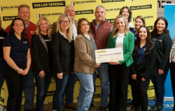 Fourteen people stand together, including members of the team from Reading is Fundamental and Dollar General. Two people hold an oversized check in the center of the group.