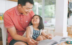 A small girl and her dad rereading and smiling at a book