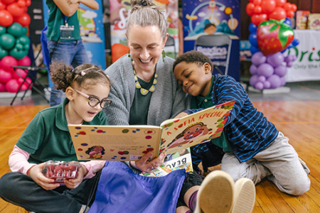 At a RIF Reading event, a seated women reads A Sofia Special to two children, a girl to her left and a boy to her right.