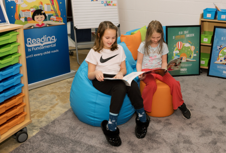 Two girls read in the new library created with the help of RIF and Dollar General. They are seated in bean bag chairs beside each other with books open. 
