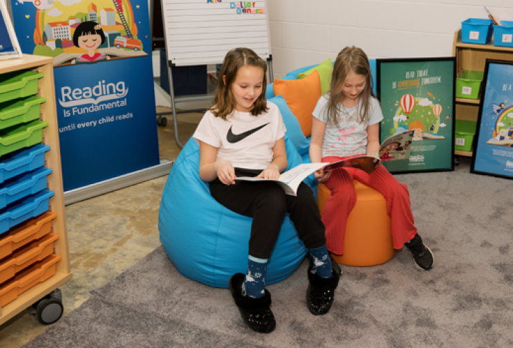 Two girls read in the new library created with the help of RIF and Dollar General. They are seated in bean bag chairs beside each other with books open.