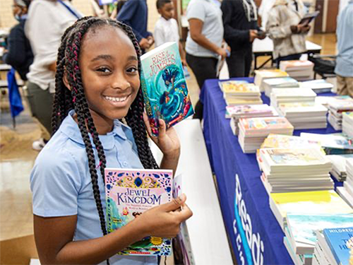 A young girl holds two books while smiling at a RIF event.